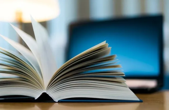 Otwarta książka przed świecącym ekranem laptopa